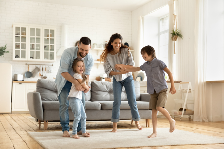 Happy family playing funny game having fun together with little son and daughter in modern living room. Young dad and mother with adorable cute children doing exercises, enjoying weekend at home.