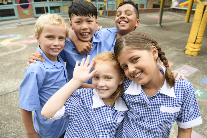 Two girls and three boys wearing school uniform smiling towards camera